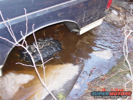 Dark blue pickup truck rear wheel well submerged in muddy water with a tire visible