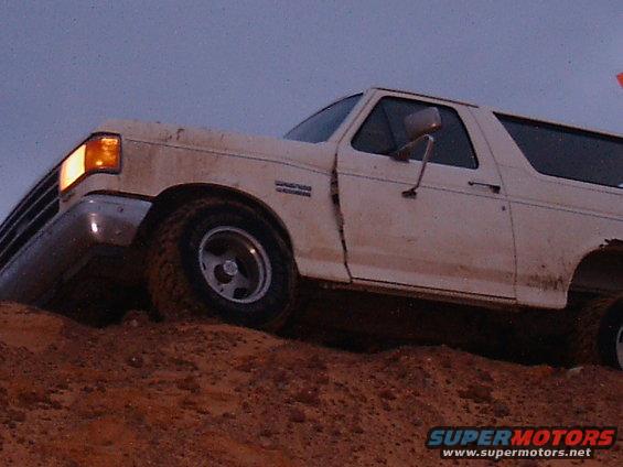 White SUV climbing a dirt hill, front wheel angled up