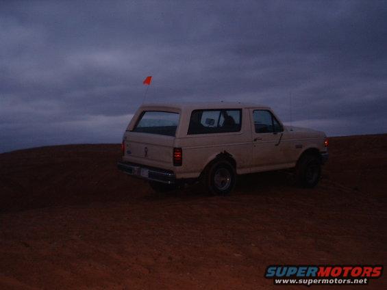Tan 1991 Ford Bronco on a sand dune under a cloudy sky