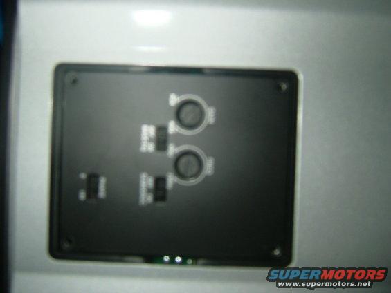 Close-up of a black aftermarket control panel with two circular knobs and several toggle switches