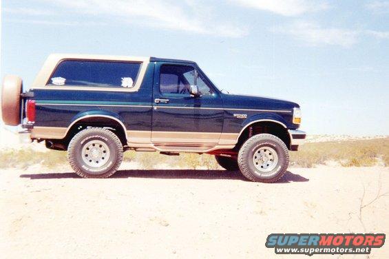 Dark green and tan Ford Bronco parked on a dirt road with a spare tire on the back