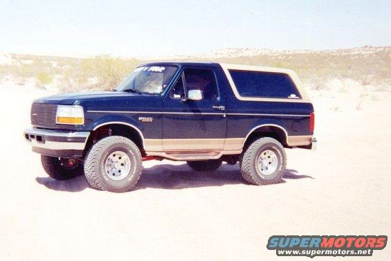 Dark blue and tan Ford Bronco parked on sand, front 3/4 view