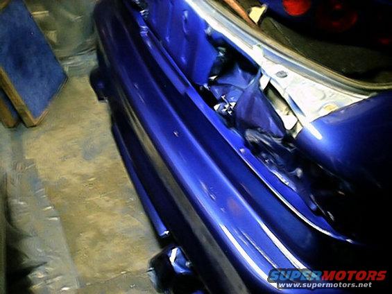 Blue car fender with open trunk showing interior panels and wiring