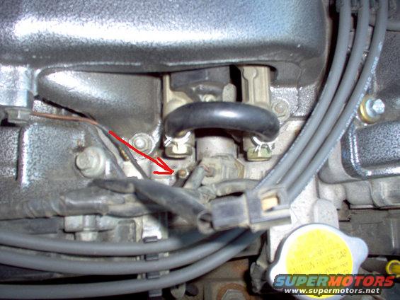 Close-up of engine components with a red arrow pointing to a small bolt