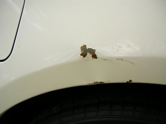 Rust spots and a dent on the rear fender of a white car, above the tire