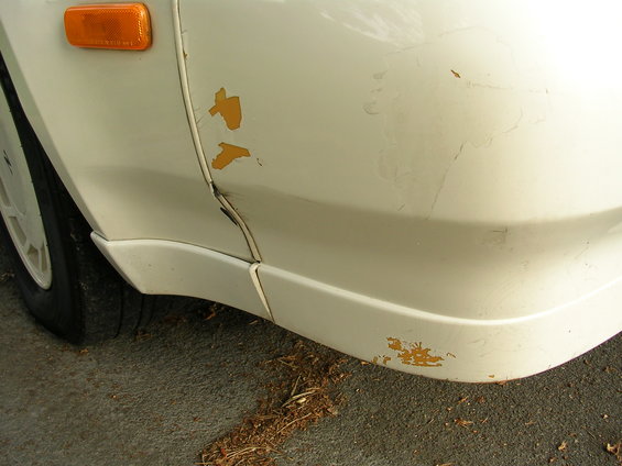 white car fender with chipped paint and dent near wheel well
