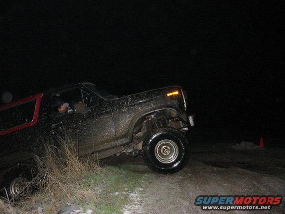 Muddy 1980s Ford Bronco off-roading at night, driver visible