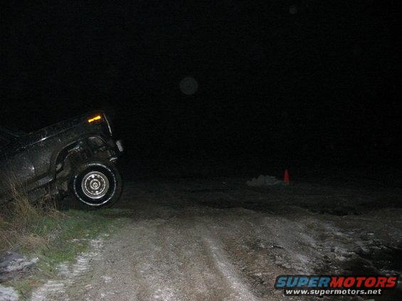 off-road vehicle stuck in a ditch at night, with a traffic cone in the distance