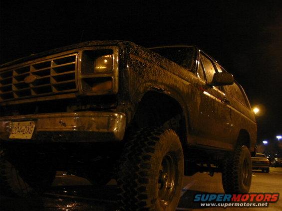 Dark 1980s Ford Bronco with large tires, viewed from a low angle at night