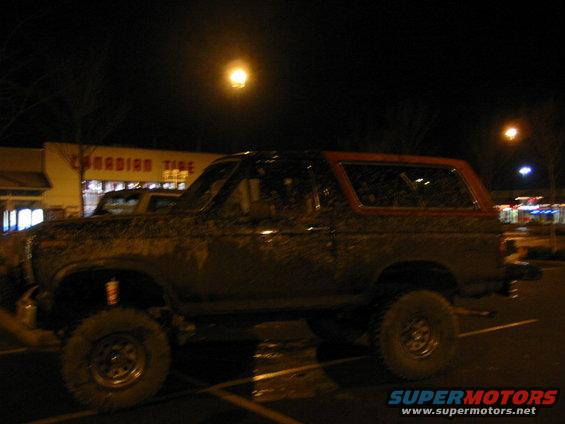 Side view of a mud-covered 1982 Ford Bronco with a red top parked at night