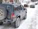 1996 Jeep Grand Cherokee - Rear view of a 1996 Jeep Grand Cherokee on a snow-covered street with other vehicles in the background.