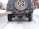 1996 Jeep Grand Cherokee - The rear of a 1996 Jeep Grand Cherokee is shown in a snowy environment, displaying its spare tire and custom bumper.