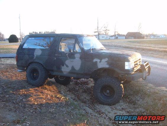 Camouflaged Ford Bronco with lifted suspension and off-road tires parked on a dirt incline