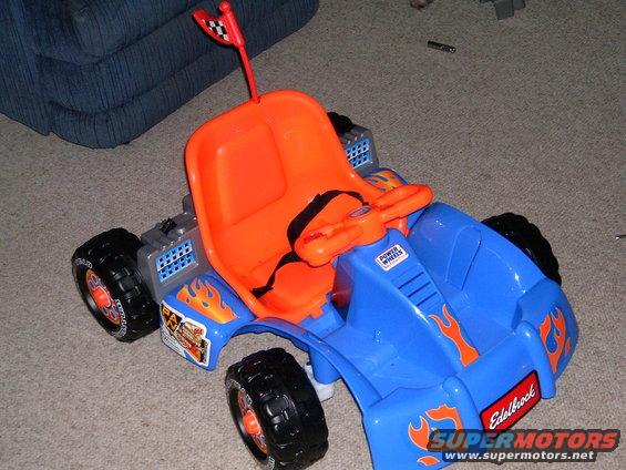 Blue and orange toy car with flame decals and a checkered flag on a stick. Has 'Power Wheels' and 'Edelbrock' labels