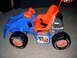 2006 Ford F1 - A blue and orange toy ride-on vehicle with flame decals and "Goodyear" tires sits on a carpeted floor.