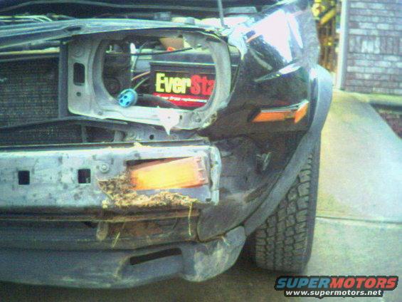 Car front end missing headlight and bumper, showing battery