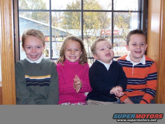 four kids smiling and looking out a window