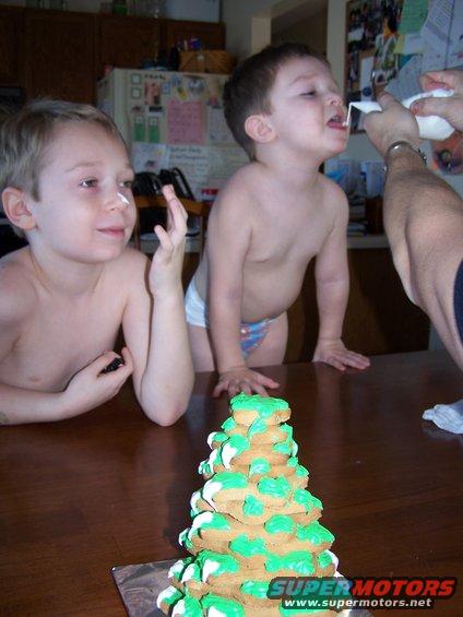 Two young boys at a table with a cookie tree; one boy has white cream on his nose