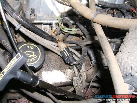 Engine bay with black oil cap, sensors, and wiring. Some dirt and grime visible