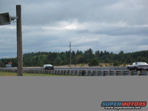 Two cars on a drag strip with a scoreboard showing 4.20