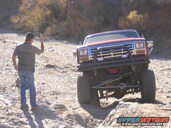Man waves at lifted Ford Bronco on rocky trail. Bronco has aftermarket bumper and grille
