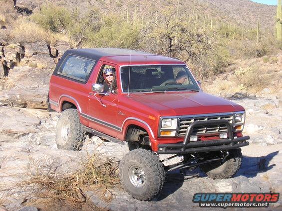 Red Ford Bronco with lifted suspension and off-road tires driving on rocks in a desert landscape