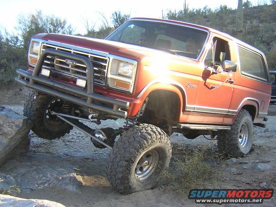 Red 1980s Ford Bronco with lifted suspension and large tires on a rocky trail