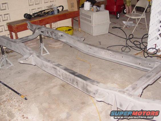 Vehicle frame on jack stands in a garage, with tools and a red cart in the background