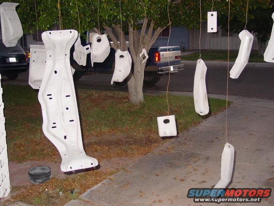 Car parts hanging from a tree to dry, with a blue pickup truck in the background