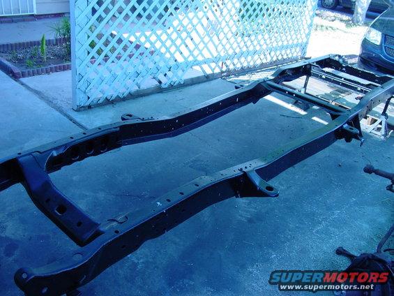 Black vehicle frame on a concrete surface with a white lattice fence in the background