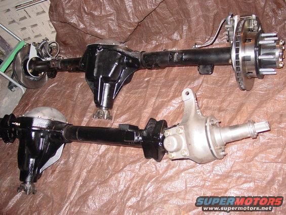 Two vehicle rear axles, one black and one silver, laid out on a brown tarp