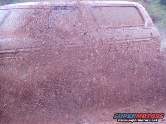 Muddy SUV driving through water, splashing water everywhere. Side view