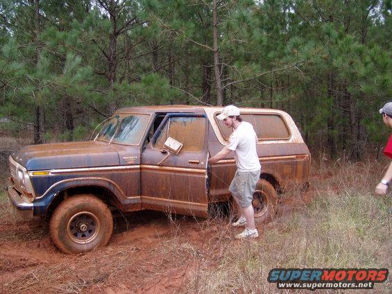Mud-covered 1978 Ford Bronco with driver's door open, stuck in mud