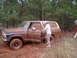 1978 Ford Bronco - A man opens the door of a mud-covered 1978 Ford Bronco stuck in a wooded area.
