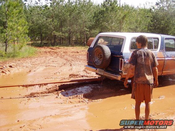 1978 Ford Bronco stuck in deep mud with a person standing nearby