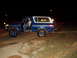 1978 Ford Bronco - A blue and white 1978 Ford Bronco is parked on uneven terrain at night, with the driver's door open.