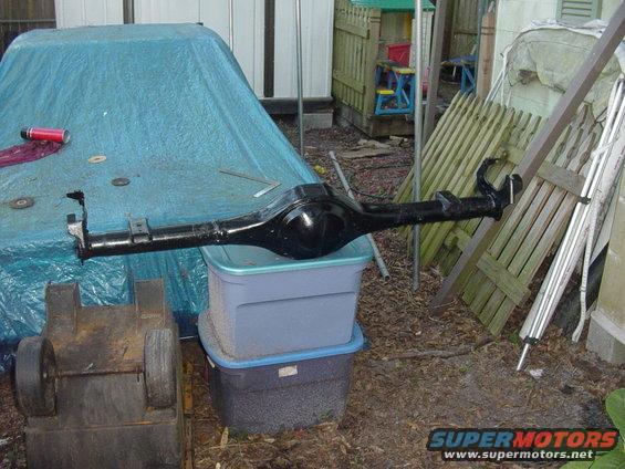 Black rear axle assembly resting on plastic bins outdoors