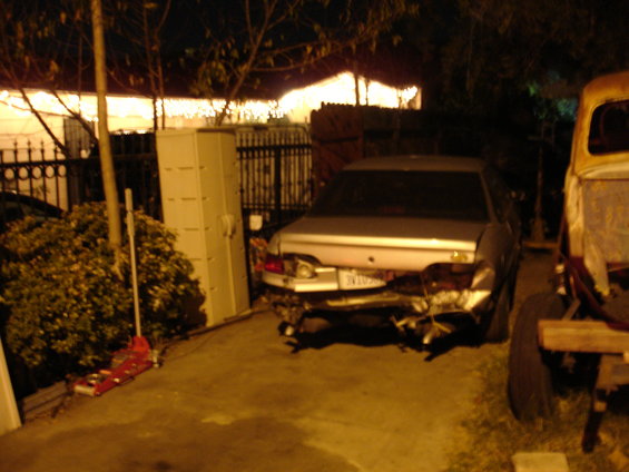 Rear view of a heavily damaged silver sedan parked next to a yellow truck