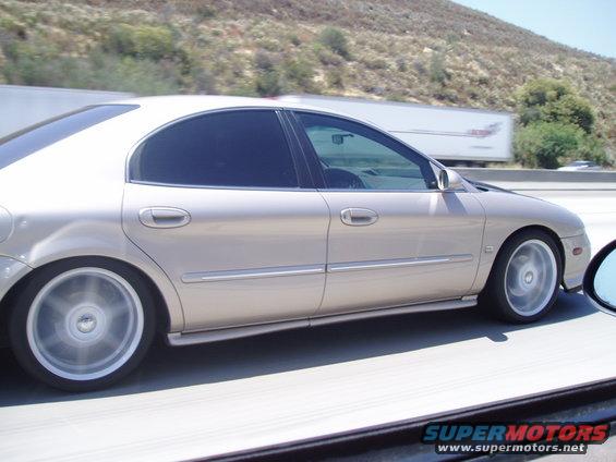 tan sedan driving on highway, side view, tinted windows, alloy wheels