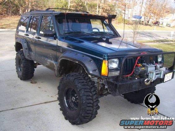 Dark green Jeep Cherokee XJ with large off-road tires and a winch on the front bumper
