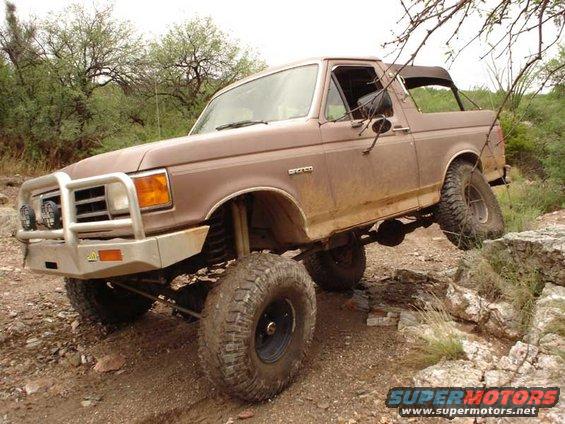 Brown 1989 Ford Bronco climbing over rocks on a dirt trail