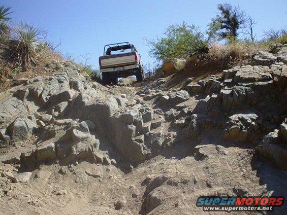 Brown and white Ford Bronco driving up a rocky hill