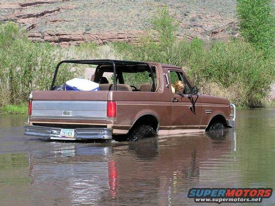Brown 1989 Ford Bronco convertible driving through water, rear view
