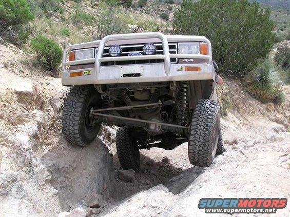 1989 Ford Bronco climbing rocks on a trail, front view with aftermarket bumper and lights