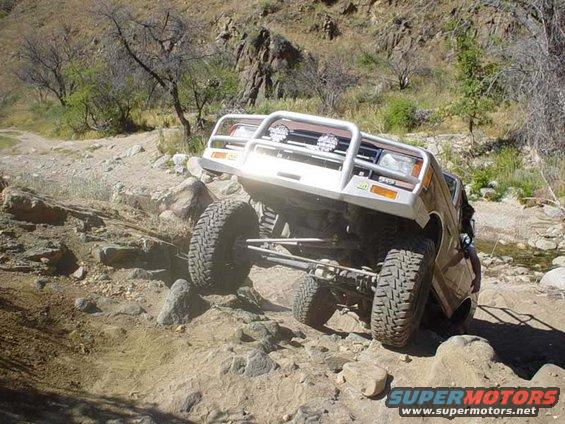Brown off-road SUV with a white bull bar and auxiliary lights navigating a rocky terrain