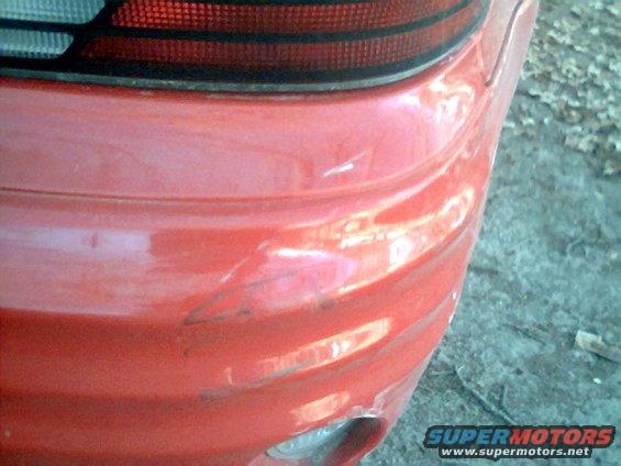Close-up of a damaged red car bumper and taillight assembly. Supermotors.net logo visible