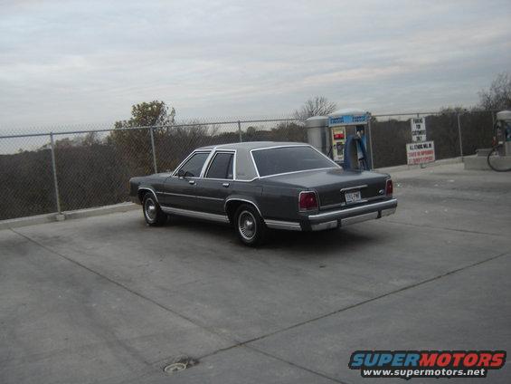 Dark sedan parked at a gas station with a chain-link fence behind it