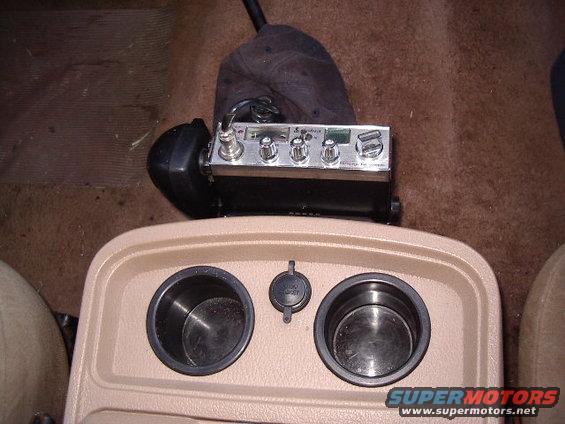 CB radio mounted above car's center console with two cup holders and a 12V power outlet