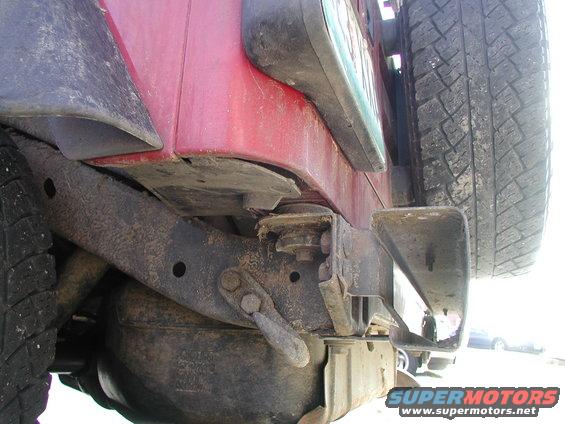 Close-up of a red Jeep Wrangler's rear bumper, showing the tire carrier and spare tire. The frame and suspension components are visible