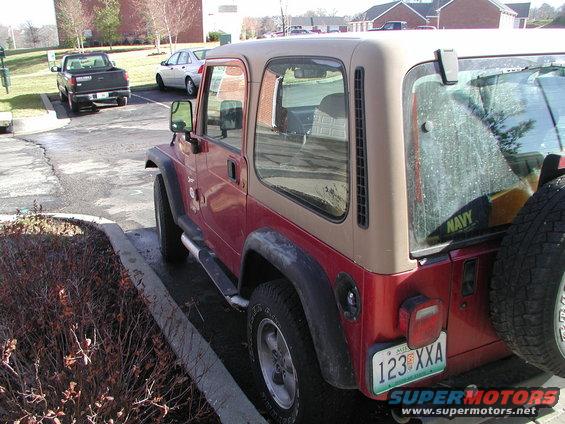 Red and tan Jeep Wrangler parked next to a curb, with a spare tire mounted on the rear